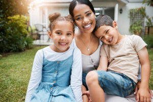 Single mother with two young children in front of house.